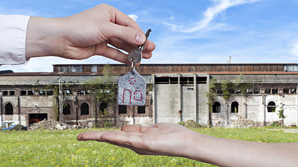 Deutschland, Menschliche Hände tauschen Hausschlüssel vor einem sehr alten und heruntergekommenen Fabrikgebäude aus - MFF000478