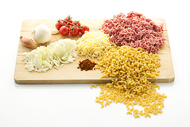 Minced meat, noodles, tomatoes, onions, garlic, cheese and spices on chopping board, close up - MAEF005712