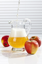 Apple juice being poured into pitcher besides apples - CSF016391