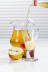 Apple juice being poured into glass besides apples and pitcher - CSF016393