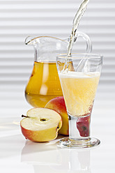 Apple juice being poured into glass besides apples and pitcher - CSF016394