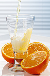 Orangenlimonade wird neben Orangen in ein Glas gegossen, Nahaufnahme - CSF016403