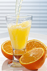 Orangenlimonade wird neben Orangen in ein Glas gegossen, Nahaufnahme - CSF016404