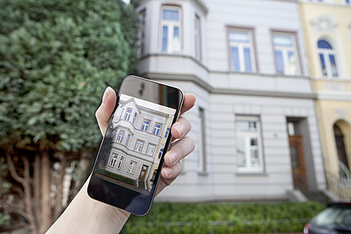 Germany, Bonn, Human hand using smart phone in front of house - MFF000479