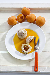 Aprikosenknödel mit gemahlenen Haselnüssen auf dem Teller und Aprikosen im Hintergrund - CSF016492