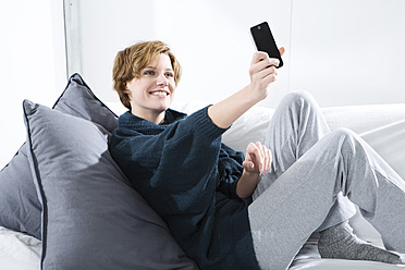 Young woman photographing with mobile on couch, smiling - MAEF005747
