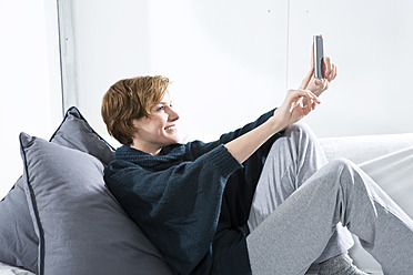 Young woman using mobile on couch, smiling - MAEF005748