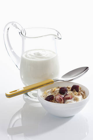 Schale mit Müsli-Joghurt mit Preiselbeeren neben Joghurt-Karaffe auf weißem Hintergrund, Nahaufnahme, lizenzfreies Stockfoto
