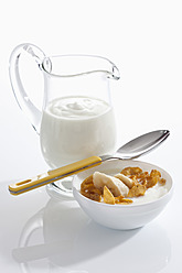 Bowl of muesli yogurt with banana beside yogurt carafe on white background, close up - CSF016567