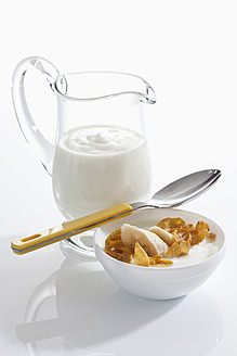 Schale mit Müsli-Joghurt mit Banane neben Joghurt-Karaffe auf weißem Hintergrund, Nahaufnahme - CSF016567