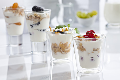 Gläser mit Joghurt, Müsli, Cornflakes und Früchten auf weißem Hintergrund, Nahaufnahme - CSF016590