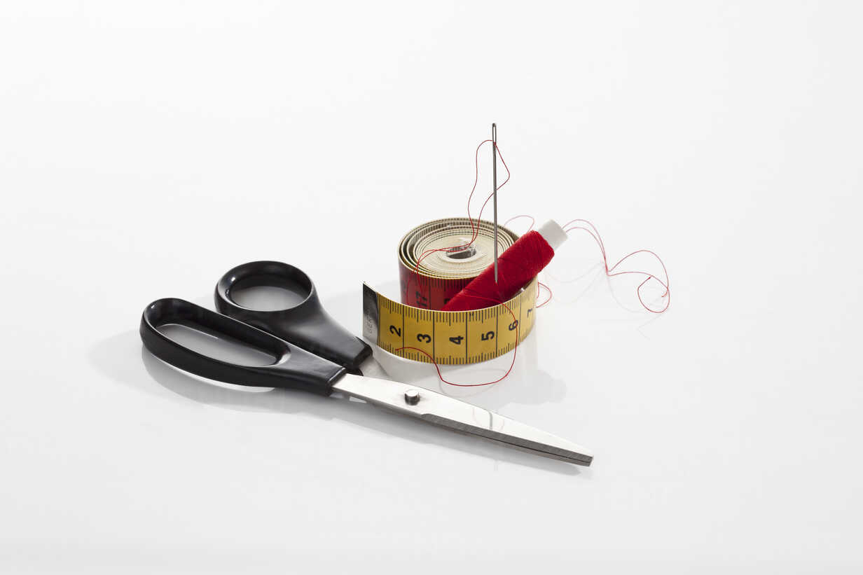 Tape measure, sewing needle and thimble against white background