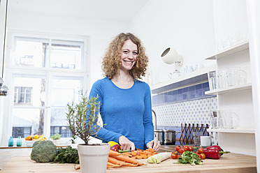 Deutschland, Bayern, München, Junge Frau schneidet Gemüse in der Küche, lächelnd, Porträt - RBF001099