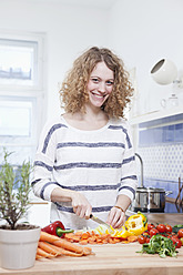 Germany, Bavaria, Munich, Young woman chopping vegetables in kitchen, smiling, portrait - RBF001102