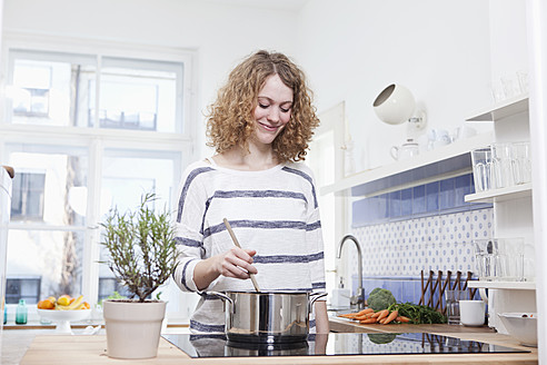 Deutschland, Bayern, München, Junge Frau beim Kochen in der Küche, lächelnd - RBF001104