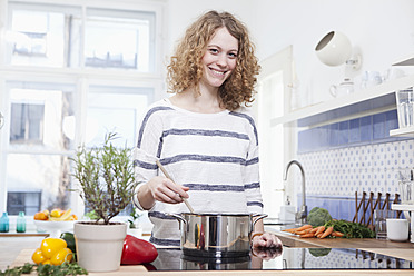 Germany, Bavaria, Munich, Young woman cooking in kitchen, smiling, portrait - RBF001105
