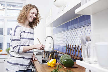 Deutschland, Bayern, München, Junge Frau beim Kochen in der Küche, lächelnd - RBF001107
