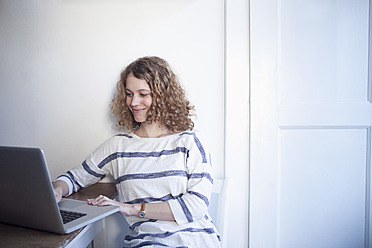 Germany, Bavaria, Munich, Young woman using laptop in kitchen, smiling - RBF001121