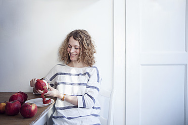 Germany, Bavaria, Munich, Young woman sitting at table and peeling apples, smiling - RBF001125