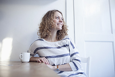 Deutschland, Bayern, München, Junge Frau sitzt am Tisch und schaut weg, lächelnd - RBF001129