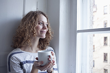 Deutschland, Bayern, München, Junge Frau schaut aus dem Fenster, lächelnd - RBF001133