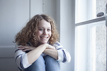 Germany, Bavaria, Munich, Young woman sitting at window, smiling, portrait - RBF001134