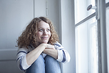 Deutschland, Bayern, München, Junge Frau sitzt am Fenster, lächelnd - RBF001136