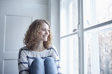 Deutschland, Bayern, München, Junge Frau sitzt am Fenster, lächelnd - RBF001141