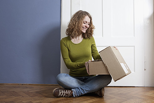 Germany, Bavaria, Munich, Young woman sitting on floor and opening postal package, smiling - RBF001143