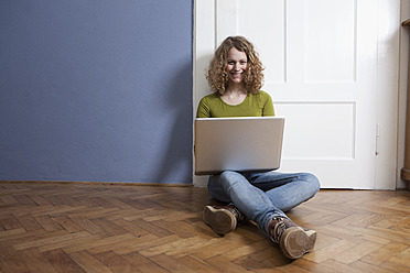 Germany, Bavaria, Munich, Young woman sitting on floor and using laptop, smiling, portrait - RBF001145