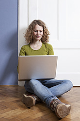 Germany, Bavaria, Munich, Young woman sitting on floor and using laptop - RBF001146