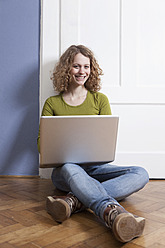 Germany, Bavaria, Munich, Young woman sitting on floor and using laptop, smiling, portrait - RBF001147