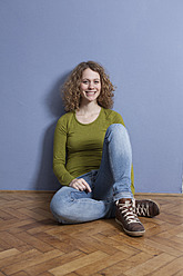 Germany, Bavaria, Munich, Young woman sitting on floor, smiling, portrait - RBF001151