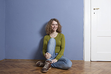 Germany, Bavaria, Munich, Young woman sitting on floor, smiling, portrait - RBF001152