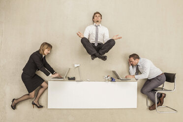 Businessman meditating above office desk while others working - BAEF000413