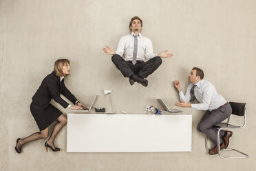 Businessman meditating above office desk while others working - BAEF000414