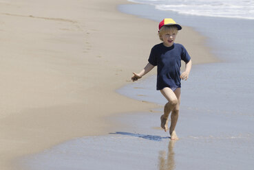 Spanien, Junge mit Schirmmütze läuft am Strand - CWF000006