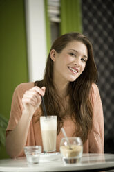 Deutschland, Bayern, München, Porträt einer jungen Frau, die lächelnd am Tisch eines Cafés sitzt - RNF001103