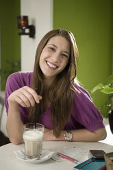 Deutschland, Bayern, München, Porträt einer jungen Frau, die in einem Café Kaffee trinkt, lächelnd - RNF001109