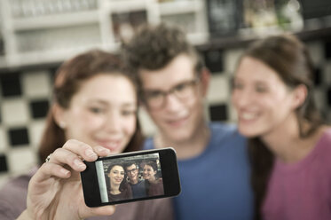 Deutschland, Bayern, München, Junge Freunde fotografieren mit Handy im Cafe - RNF001137