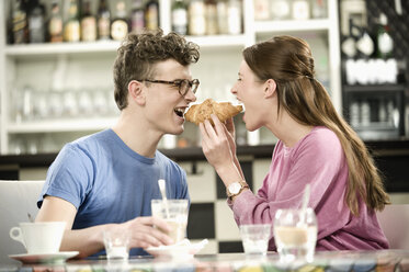 Germany, Bavaria, Munich, Young man and woman sharing croissant in cafe - RNF001125