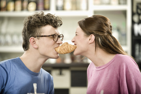 Deutschland, Bayern, München, Junger Mann und Frau teilen sich ein Croissant im Cafe, lizenzfreies Stockfoto