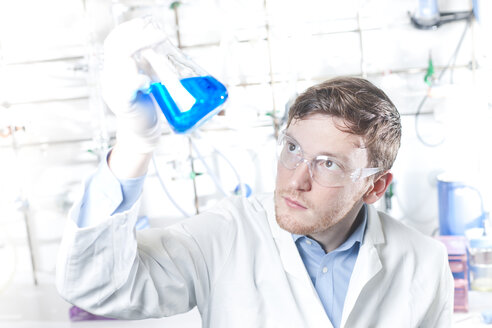 Germany, Young scientist checking blue liquid in erlenmeyer flask - FLF000230