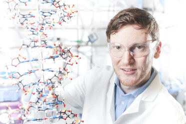 Deutschland, Porträt eines jungen Wissenschaftlers mit DNA-Modell, lächelnd - FLF000243