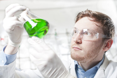 Germany, Young scientist checking green liquid in erlenmeyer flask - FLF000244