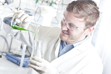 Germany, Young scientist pouring green liquid into erlenmeyer flask - FLF000262