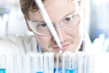 Germany, Young scientist pipetting blue liquid into test tubes, close up - FLF000264