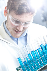 Germany, Young scientist pipetting blue liquid into test tubes, close up - FLF000267
