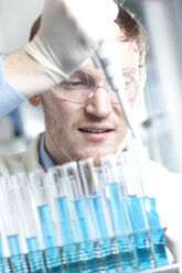 Germany, Young scientist pipetting blue liquid into test tubes, close up - FLF000268