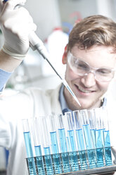 Germany, Young scientist pipetting blue liquid into test tubes, close up - FLF000269